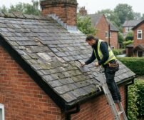 A roofer inspecting slate tiles on a Cheshire home to assess whether a roof repair or full replacement is needed.