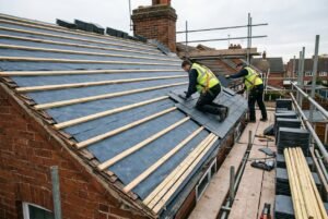 Roofers on scaffolding during a roof replacement, showing the stages of laying underlay, timber battens, and new slate tiles.